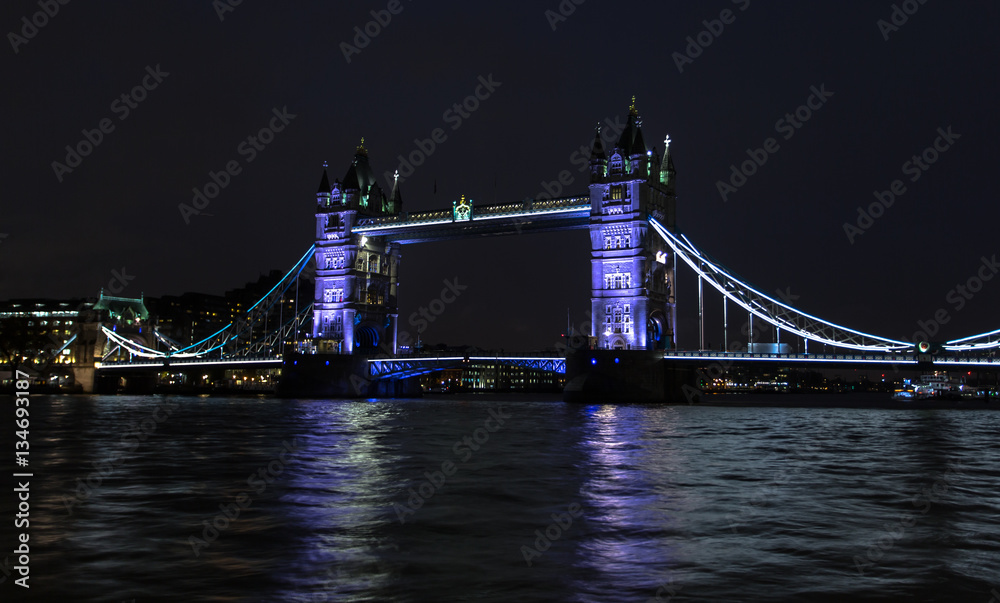 Fototapeta premium London Bridge illuminated at night. Colorful lights, urban skyline, Thames River reflection, travel and cityscape photography.