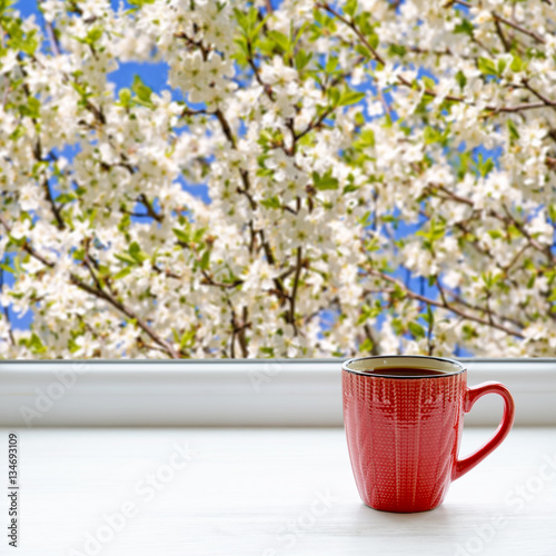 Coffee cup on a windowsill. Blooming apple tree outside the window