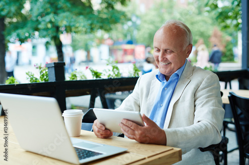 Pleased Senior Looking at Tablet Screen photo