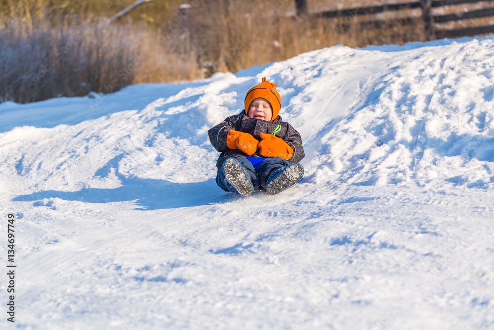 Happy little caucasian boy downhill on plastic slider or sledge