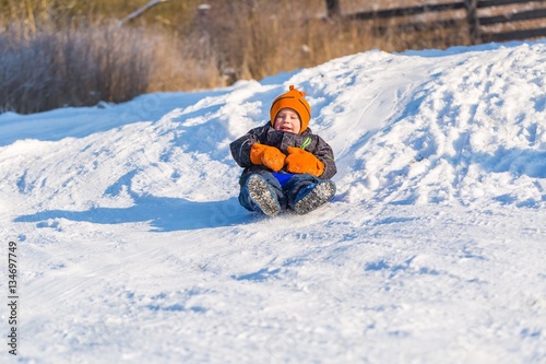 Happy little caucasian boy downhill on plastic slider or sledge