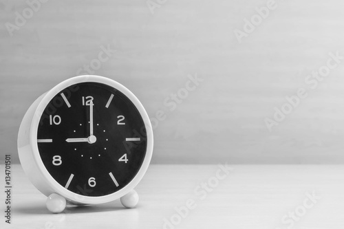 Closeup alarm clock for decorate in 9 o'clock on wood desk and wall textured background in black and white tone with copy space