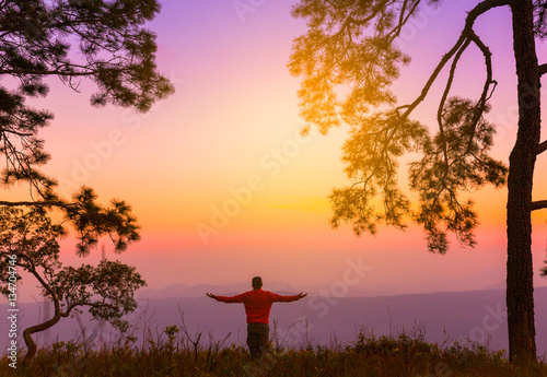 Silhouette of young man on sunset or sunrise in pine forest. Con