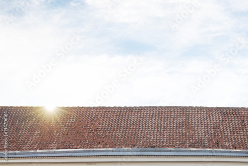 cloudy blue sky with sun flares, tiled roof top background