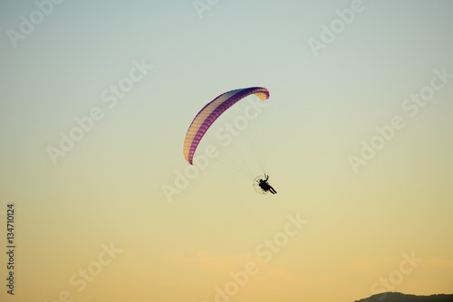 paramotor glider flying in the sky over beautiful countryside field landscape at sunset