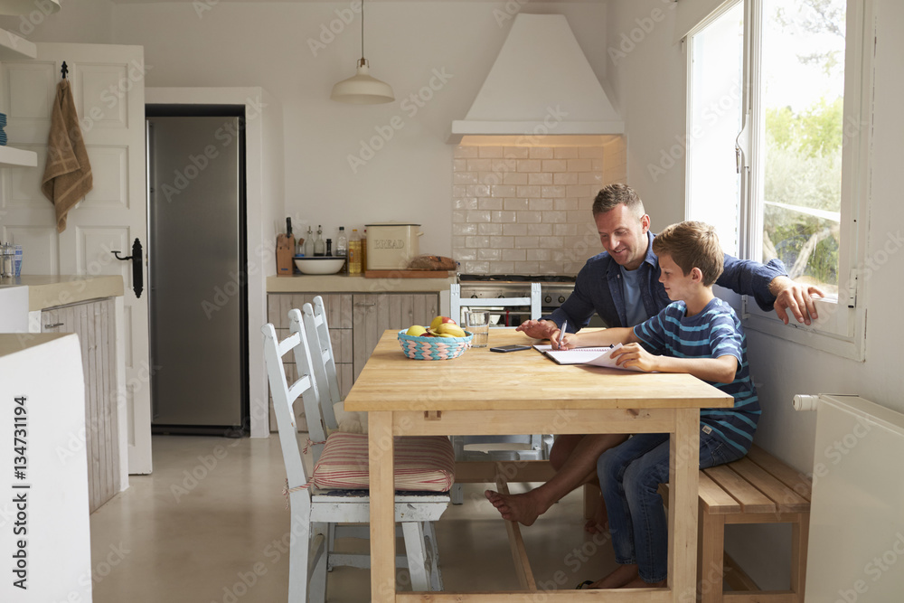 Father Helping Son With Homework Sitting At Kitchen Table