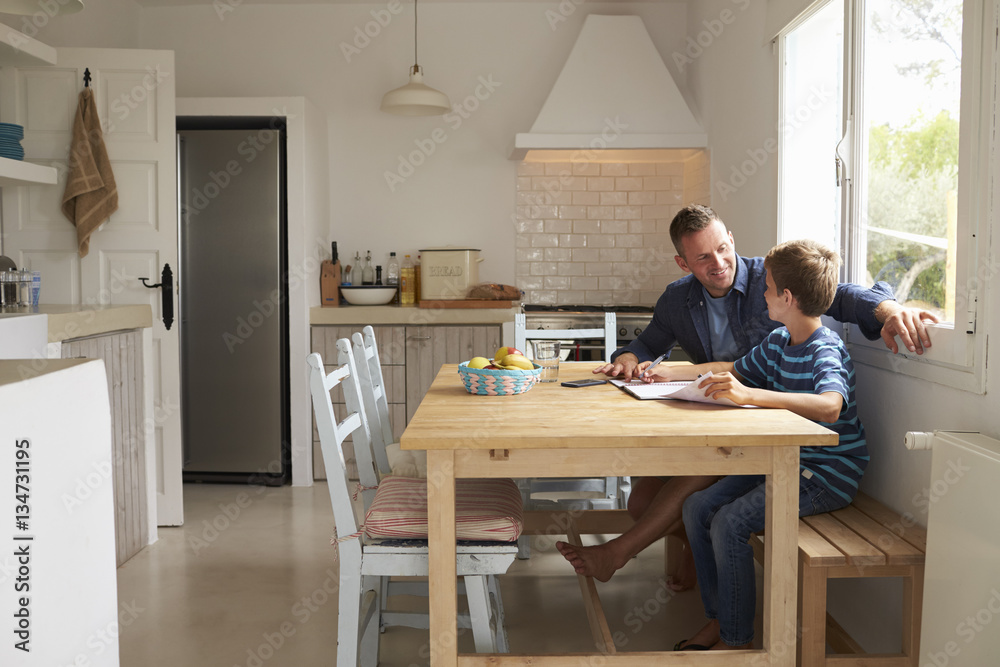 Father Helping Son With Homework Sitting At Kitchen Table Father Helping Son With Homework Sitting At Kitchen Table