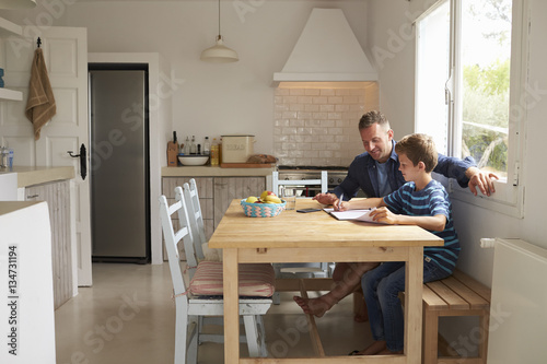 Father Helping Son With Homework Sitting At Kitchen Table