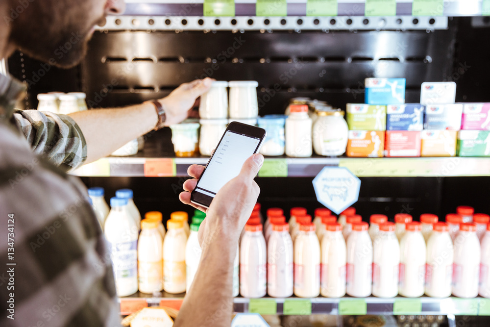 Obraz premium Man using mobile phone on shopping at grocery shop
