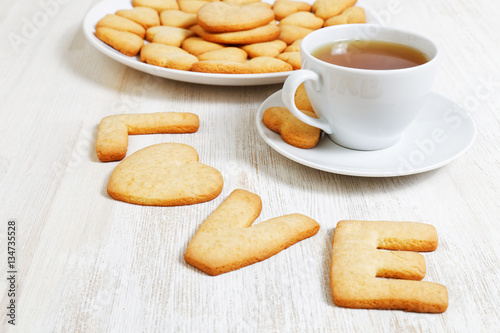 LOVE-shaped cookies and a white cup of tea on white wooden table. Cookies for Valentines Day.