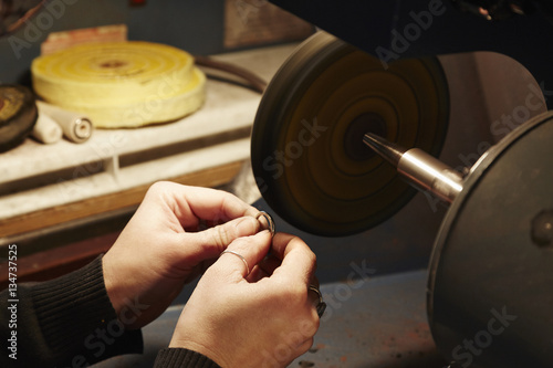 A person holding a small ring and using a grinding machine to shape and polish it. Workbench in a jewellers.  photo