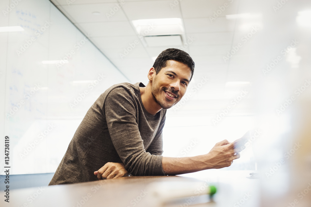 A young man sitting in a classroom leaning on a desk and smiling. A young man sitting in a classroom leaning on a desk and smiling.