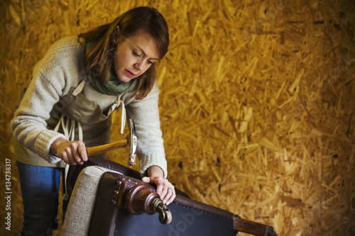 Upholstery workshop. An upholsterer using a hammer to secure fabric and padding to a chair leg. 