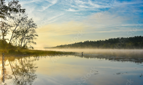 Brilliant and bright mid-summer sunrise on a lake.   Warm water and cooler air at daybreak creates misty fog patches.  Still water along a calm, quiet Ontario lakeside.  © valleyboi63