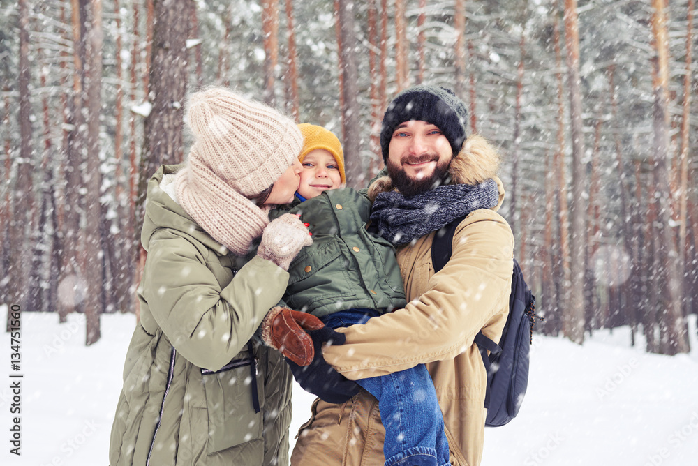 Smiling family hugging son and looking at the camera under snowf