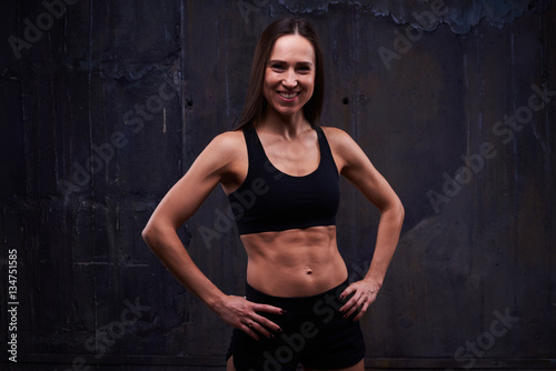Smiling muscular trainer woman posing against black background © ArtFamily