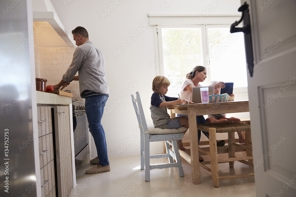 Dad cooking and mum with kids at kitchen table, low angle