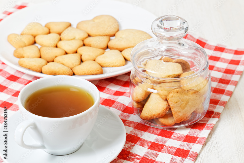 Heart-shaped cookies and a white cup of tea on white wooden table. Treat for Valentines Day. Heart-shaped cookies and a white cup of tea on white wooden table. Treat for Valentines Day.