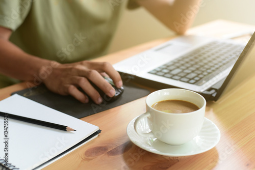 Close up of white coffee cup and hands of man working with computer