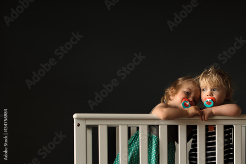 Twin sisters in cot with dummies 