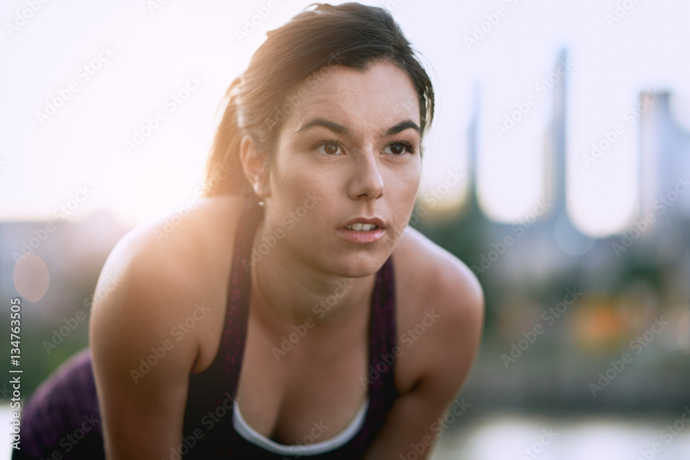 Portrait of active millenial woman jogging at dusk with an urban cityscape and sunset in the background Portrait of active millenial woman jogging at dusk with an urban cityscape and sunset in the background