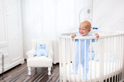Baby boy standing in bed in white nursery