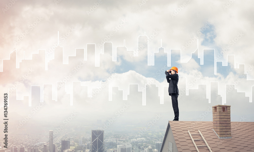 Engineer man standing on roof and looking in binoculars. Mixed m Engineer man standing on roof and looking in binoculars. Mixed m