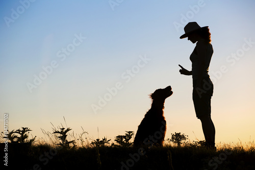 Silhouette of a female as training her dog. Pet training concept.