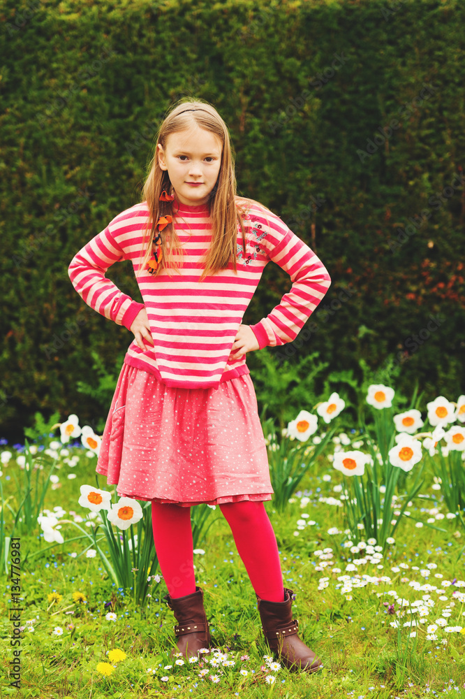 Cute little girl of 7-8 years old playing in the spring park between daffodils flowers, wearing stripe pullover, red skirt and tights, brown leather boots Cute little girl of 7-8 years old playing in the spring park between daffodils flowers, wearing stripe pullover, red skirt and tights, brown leather boots