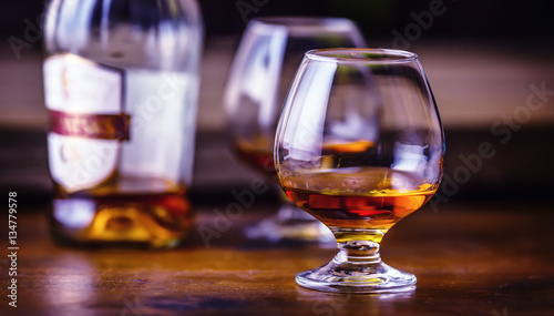 Glass whiskey cognac brandy or rum.One half full glasses of cognac on a wooden surface.