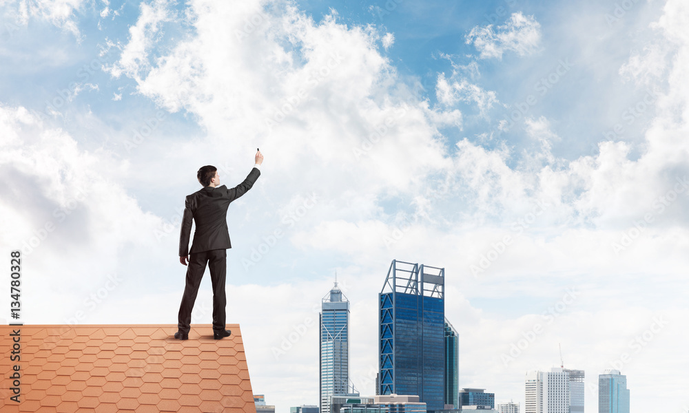 Businessman on house roof touch empty space. Mixed media Businessman on house roof touch empty space. Mixed media