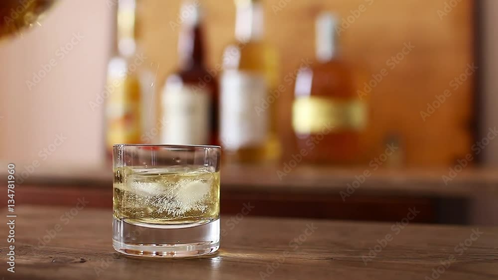 Pour whiskey into a glass placed on a wooden table Pour whiskey into a glass placed on a wooden table