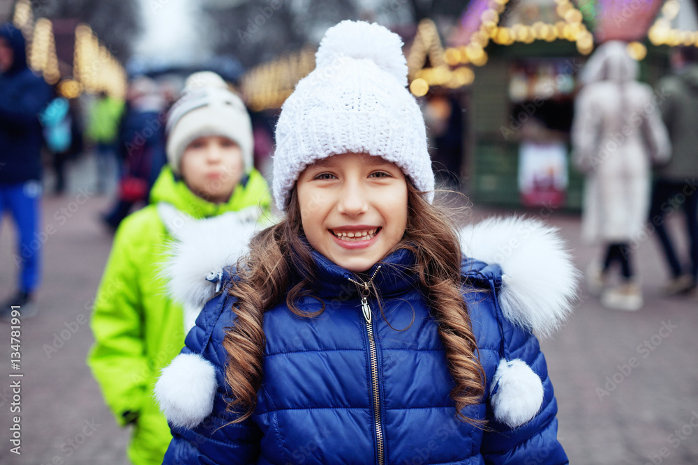 Happy child girl in a jacket and hat walking around the city. 