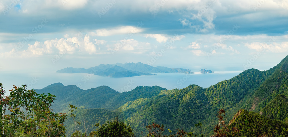 Panoramic view of blue sky, sea and mountain seen from Cable Car viewpoint, Langkawi Island, Malaysia. Tropical trees in the foreground.