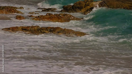 Beautiful white bubbles created on the beach by ocean waves on seashore. The ocean waves hit the rocks on the beach.