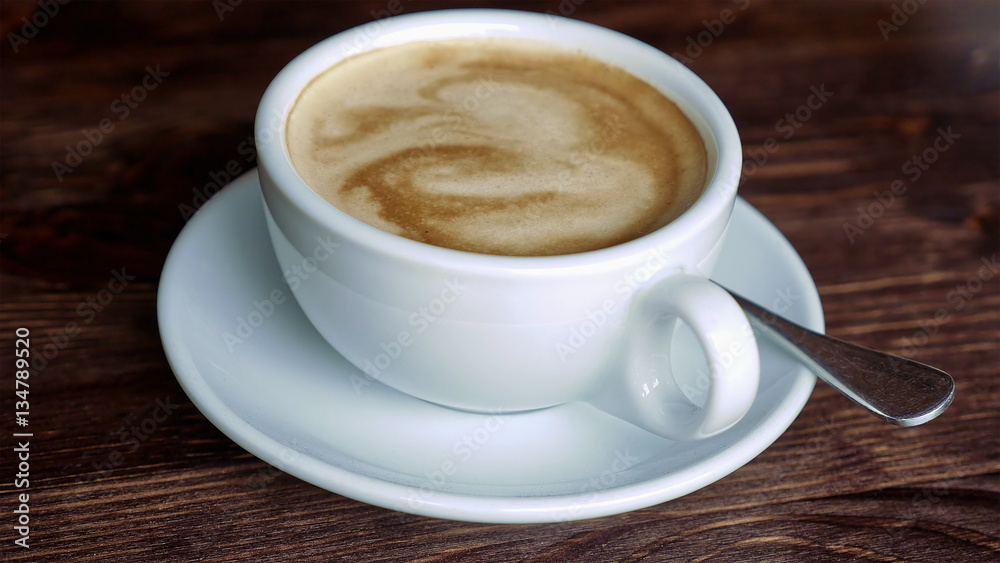 White cup with coffee, saucer and teaspoon on wooden table surface. Close-up. White cup with coffee, saucer and teaspoon on wooden table surface. Close-up.