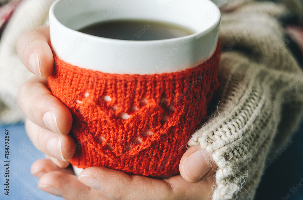 Red Knitted woolen cup with heart pattern in female hands. Hands holding a cozy Mug in red knitted mitten with hot cocoa, tea or coffee. Hands in warm concept Red Knitted woolen cup with heart pattern in female hands. Hands holding a cozy Mug in red knitted mitten with hot cocoa, tea or coffee. Hands in warm concept