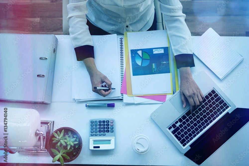 Businesswoman using laptop while writing on notepad Businesswoman using laptop while writing on notepad
