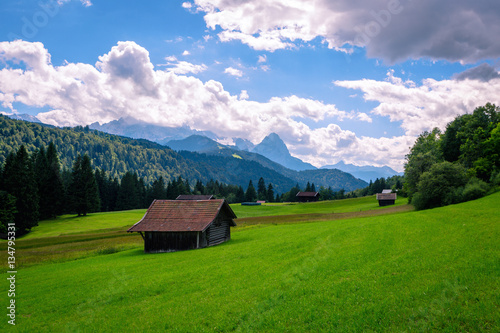 Beautiful view of idyllic mountain scenery in the Alps with traditional chalet and fresh green pastures blooming flowers on a sunny day blue sky clouds in summer