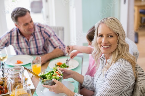 Smiling woman holding bowl of salad on dinning table