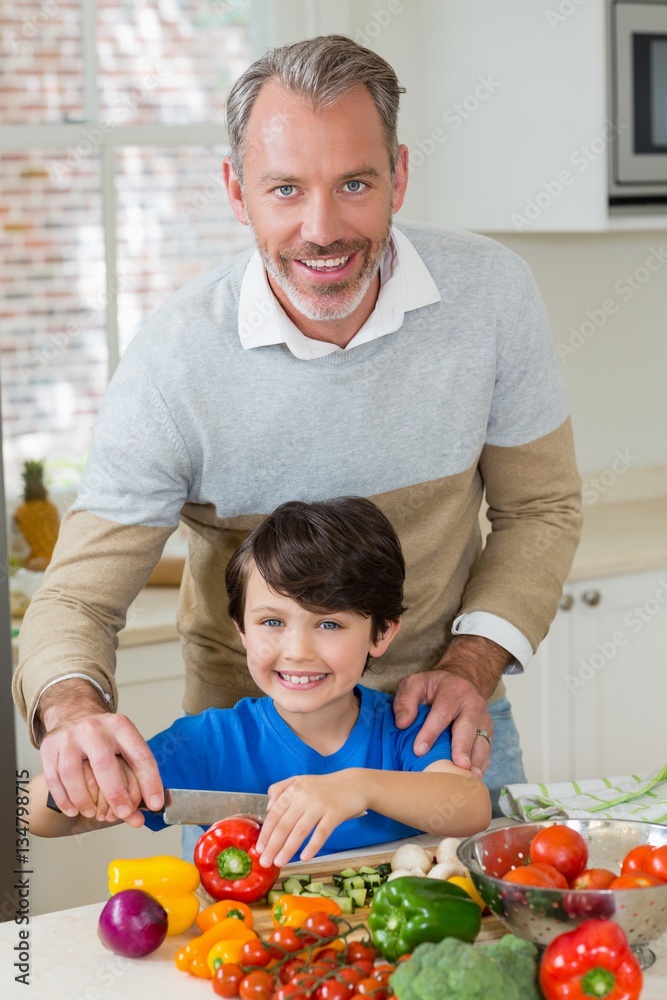 Father assisting a son to chop the red bell pepper in kitchen Father assisting a son to chop the red bell pepper in kitchen