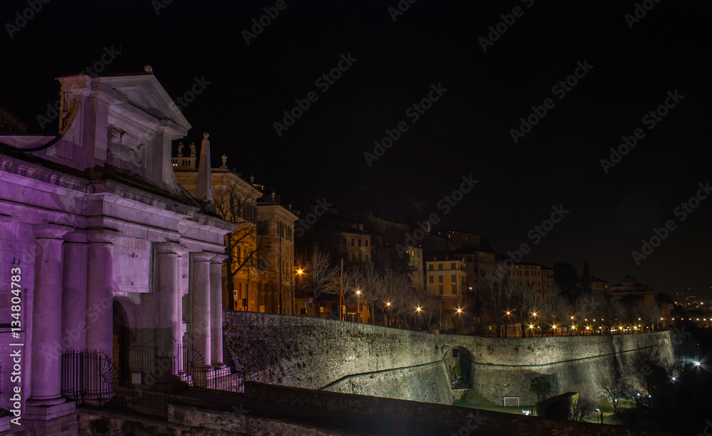 Bergamo - Old city (Citta Alta). One of the beautiful city in Italy. Lombardia. Landscape on the old gate named Porta San Giacomo during the night illuminated pink color. Venetian walls of Bergamo.