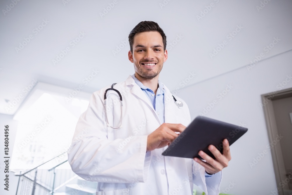Portrait of smiling doctor using digital tablet in corridor Portrait of smiling doctor using digital tablet in corridor