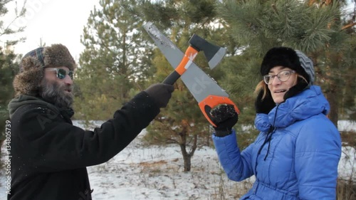 Strange man in a hipster sunglasses with beard and woman in a hat crossed saw and axe.