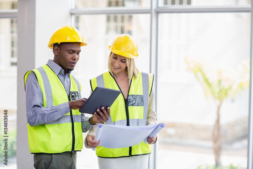 Architects holding blueprint discussing over digital tablet Architects holding blueprint discussing over digital tablet