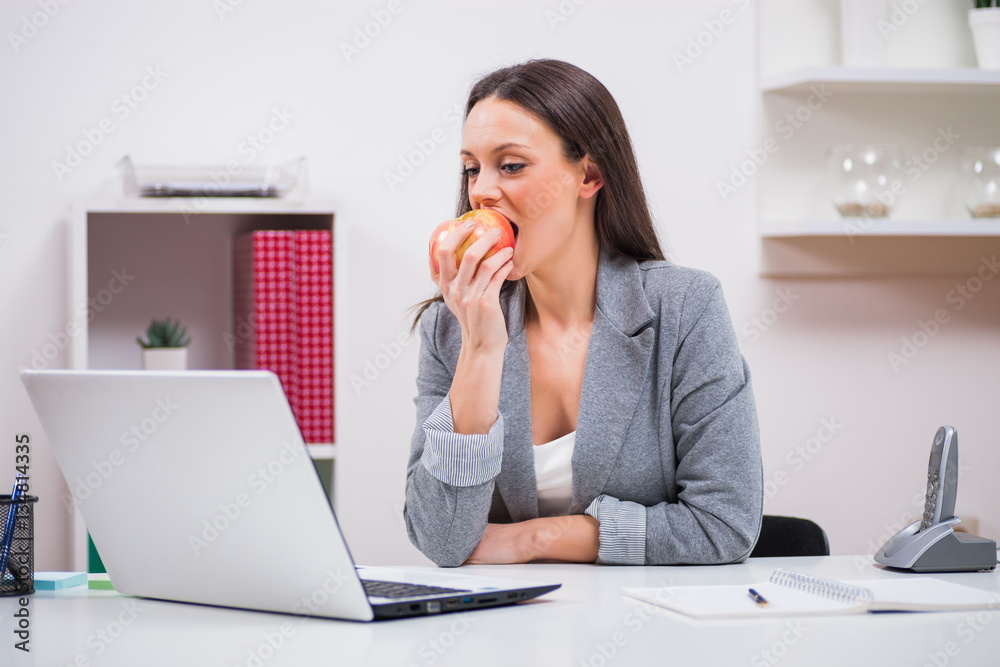 Young businesswoman is eating apple in her office.