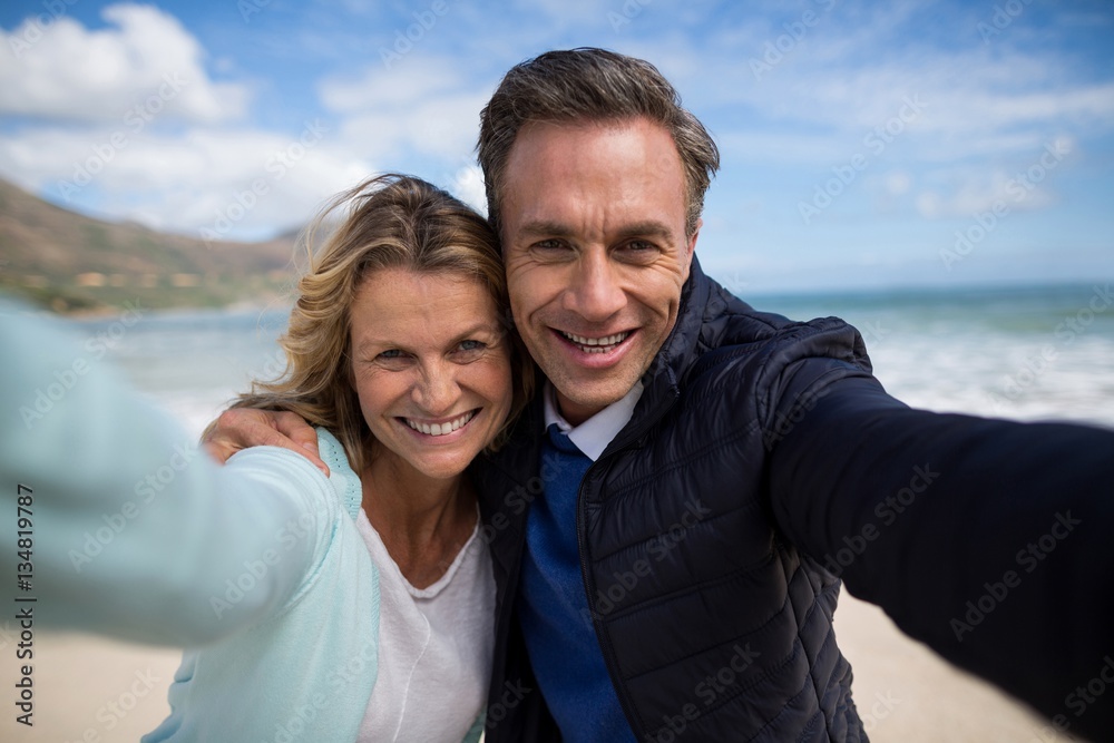 Mature couple smiling at camera on the beach - obrazy, fototapety, plakaty 