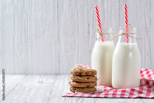 Bottles of milk with red striped straws and chocolate chip cookies on wooden background photo