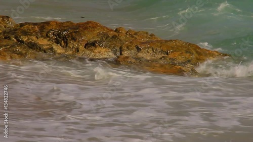 Beautiful white bubbles created on the beach by ocean waves on seashore. The ocean waves hit the rocks on the beach.