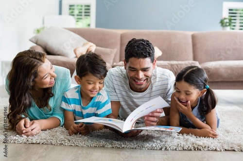 Mixed race parents and children lying on rug reading book 